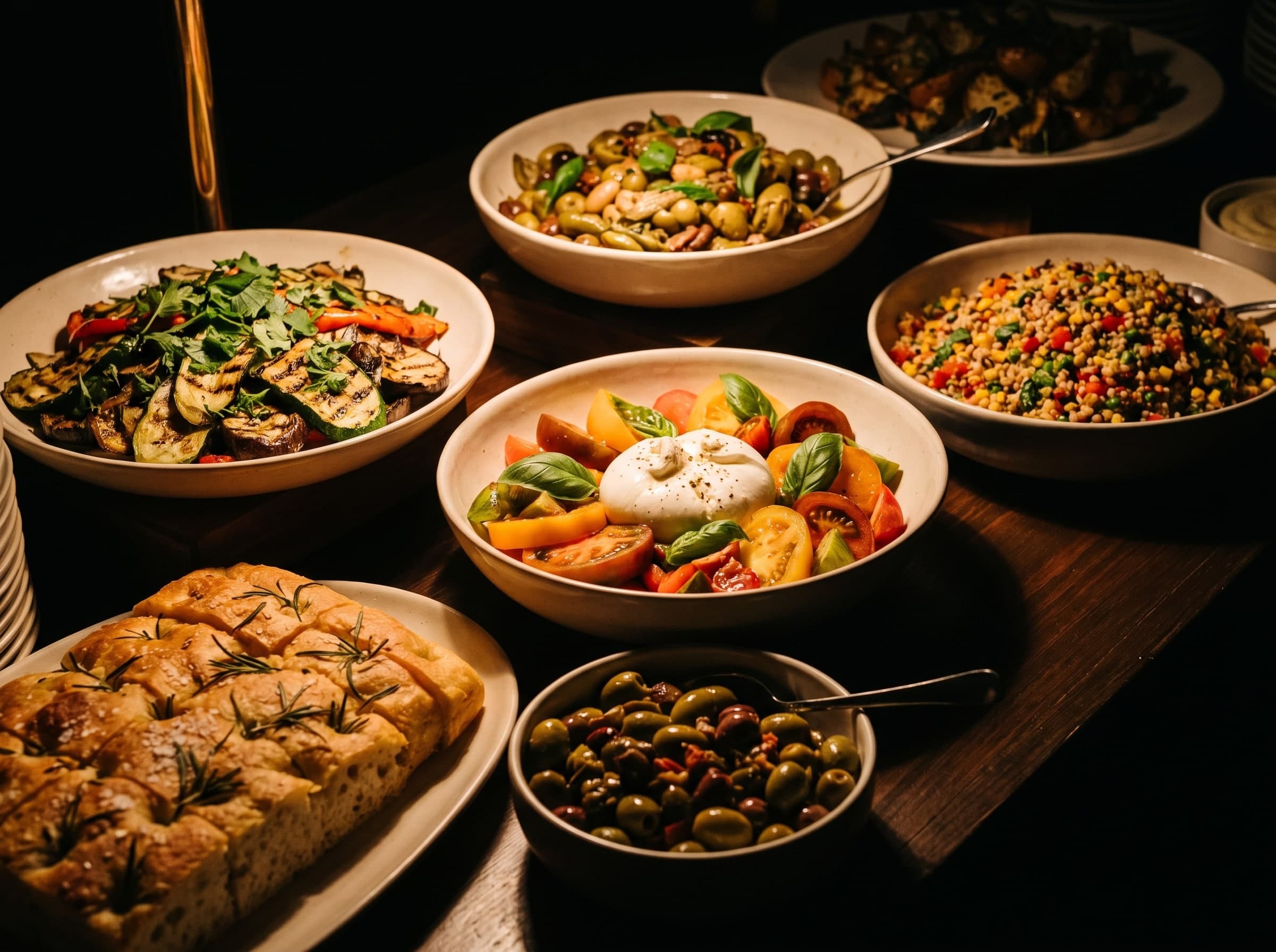 Buffet mit Schalen voll gegrilltem Gemüse, Burrata-Salat, Rosmarin-Focaccia, Oliven und Getreidesalat